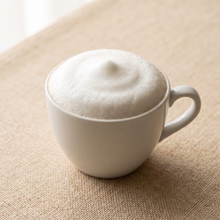 Cappuccino dalam cup keramik putih dengan lapisan foam susu tebal.